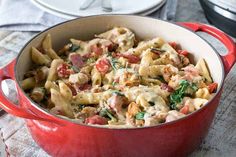 a red pot filled with pasta and meat on top of a wooden table next to an oven