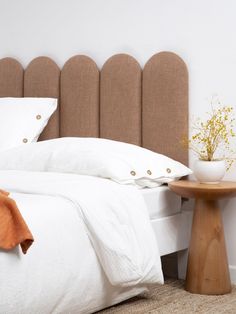 a bed with white linens and brown headboard next to a small wooden table