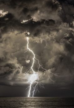 a lightning bolt striking over the ocean on a cloudy day with black and white clouds