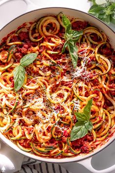 a pan filled with pasta and sauce on top of a white table next to basil leaves