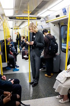 a woman standing on a subway looking at her cell phone while others sit and stand around