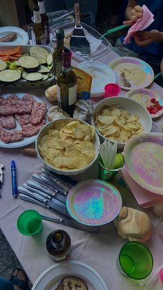 a table filled with plates and bowls full of food next to wine bottles, utensils and other items