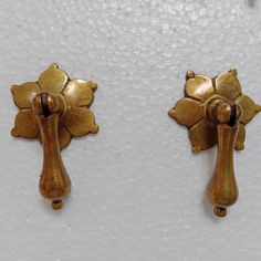 two gold colored metal objects on a white surface, one is shaped like a cross and the other is shaped like a flower