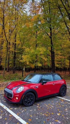 a small red car parked in a parking lot next to trees with leaves on them