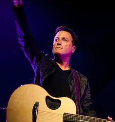 a man holding an acoustic guitar in his right hand and raising his left arm up