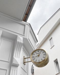 a clock hanging from the side of a white building next to a door and window