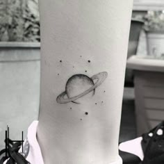 a black and white photo of a small saturn tattoo on the right leg, with stars all around it