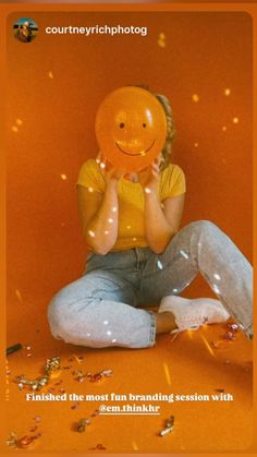 a person sitting on the ground with an orange balloon in front of their face and confetti falling around them