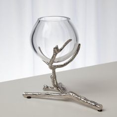 a glass with branches in it sitting on a table next to a metal branch holder