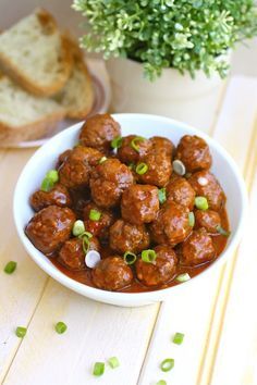 a bowl filled with meatballs sitting on top of a wooden table next to bread