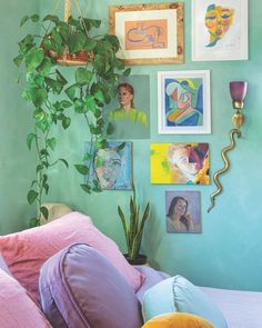 a bedroom with green walls and pictures on the wall, plants are hanging above the bed