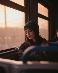 a woman reading a book while sitting on a subway car with the sun shining through the window