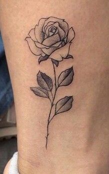 a small rose tattoo on the side of a woman's leg, with leaves