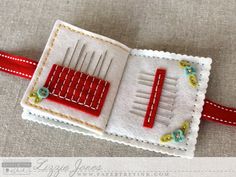 a red and white piece of fabric with pins in it on top of a table