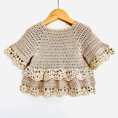 a crocheted sweater hanging on a wooden hanger