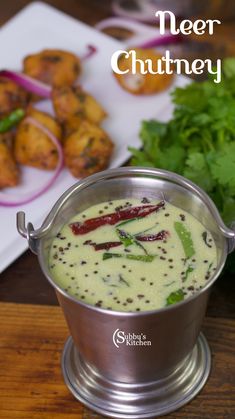 a silver bowl filled with food on top of a wooden table next to other foods