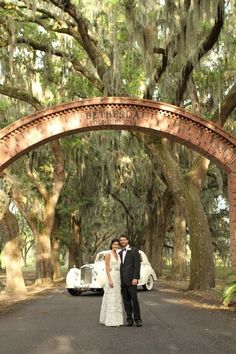 a bride and groom standing in front of an old - fashioned car under the trees