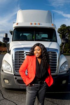 a woman standing in front of a semi truck with her hands on her hips and smiling at the camera