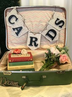 a suitcase filled with books and flowers on top of a table next to a card game