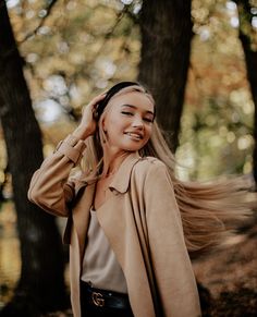 a woman standing in the woods with her hair blowing in the wind and smiling at the camera