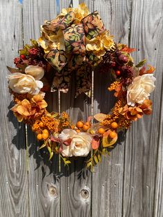 a wreath with oranges and yellow flowers hanging on a wooden fence next to an umbrella