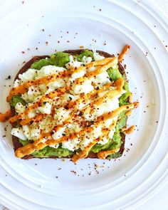 a white plate topped with an open face sandwich covered in cheese and other toppings