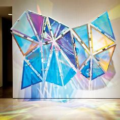 an abstract sculpture is displayed in front of a white wall with multicolored glass panels