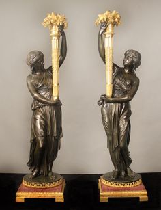 two statues of women holding vases with flowers in their hands, one is gold and the other is silver