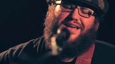 a bearded man wearing glasses and a hat singing into a microphone