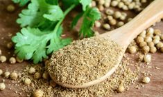 a wooden spoon filled with spices next to corian seeds and parsley on a table