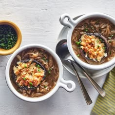 two white bowls filled with soup next to spoons