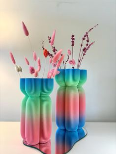 two colorful vases with flowers in them on a white table next to each other