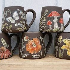 four coffee mugs with painted flowers and butterflies on them are sitting on a shelf