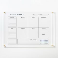 a weekly planner on a white board with gold pins attached to the back of it