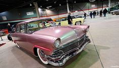 an old car is parked in a showroom with people looking at the cars on display