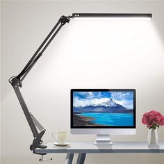 a desk with a monitor, keyboard and cup on it next to a lamp that is turned on