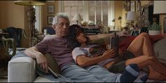 an older man sitting on a couch next to a young woman with her arm around him