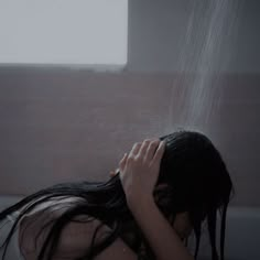 a woman is sitting in the shower with her hands on her head