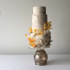 a three tiered white cake with yellow flowers on the top and bottom, sitting on a silver pedestal