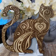 an intricately designed wooden cat sitting on top of a table next to white flowers