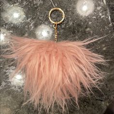 a pink furry animal keychain hanging from a metal hook on a marble surface