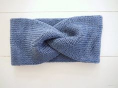 a blue knitted headband with a knot on the front and side, sitting on a white surface