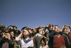 a group of people looking up into the sky with binoculars in their hands and wearing hats