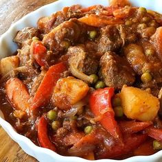 a white bowl filled with meat and vegetables on top of a wooden table next to a fork