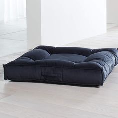 a black dog bed sitting on top of a hard wood floor next to a white wall