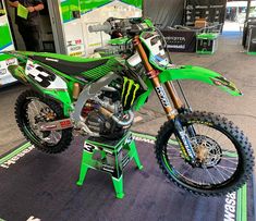 a green dirt bike sitting on top of a table next to a man in a black shirt