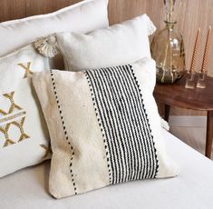 three decorative pillows on a white bed with black and gold trimmings, along with candles