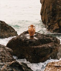 a vase sitting on top of a rock next to the ocean with waves crashing around it