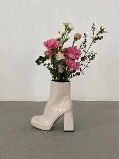 a white boot with pink and white flowers in it sitting on the ground next to a wall