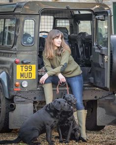 a woman sitting on the back of a truck with two dogs in front of her